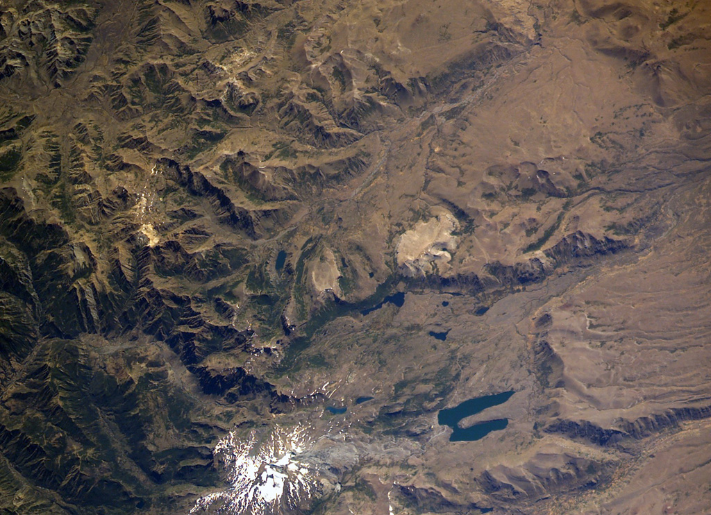 The small snow-free crater at the upper right, above and to the right of the light-colored area just right of the center of this NASA International Space Station image (with north to the upper left) is Trolon volcano. It lies in Argentina NE of the Caldera del Agrio (lower right), whose floor contains several lakes, including the U-shaped one at lower right near the SE caldera wall.  Trolon is a lava-dome complex with two summit craters and a pyroclastic cone.  Snow-covered Copahue volcano (bottom left-center) overlies the western rim of Caldera del Agrio. NASA International Space Station image ISS006-E-39998, 2003 (http://eol.jsc.nasa.gov/).