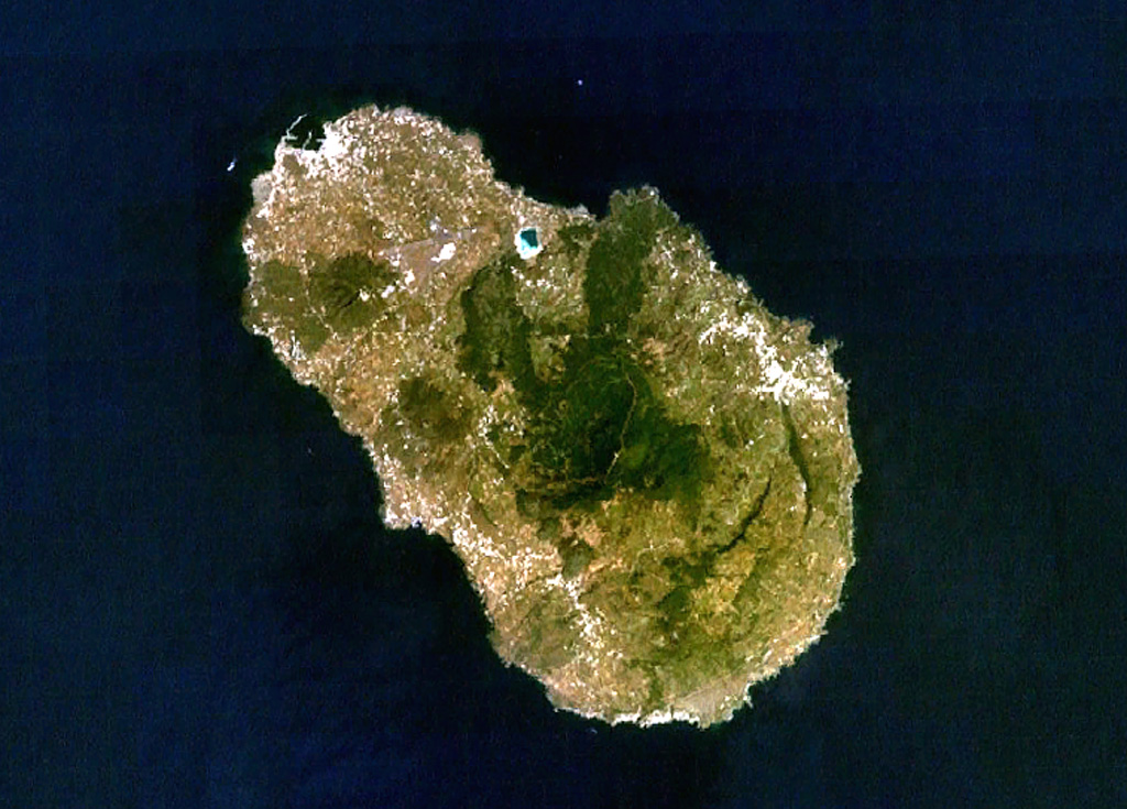 The 15-km-long island of Pantelleria is constructed above a drowned continental rift in the Strait of Sicily. Part of the mostly buried arcuate rims of two large Pleistocene calderas are seen in this NASA Landsat image (with N to the top). The SE rims of the calderas form the two dark-colored lines at the lower right part of the island, below and to the right of the forested Monte Grande and Monte Gibele volcanoes. Monte Gibele, with its circular summit crater, was constructed in the southern part of the younger Cinque Denti caldera. NASA Landsat 7 image (worldwind.arc.nasa.gov)