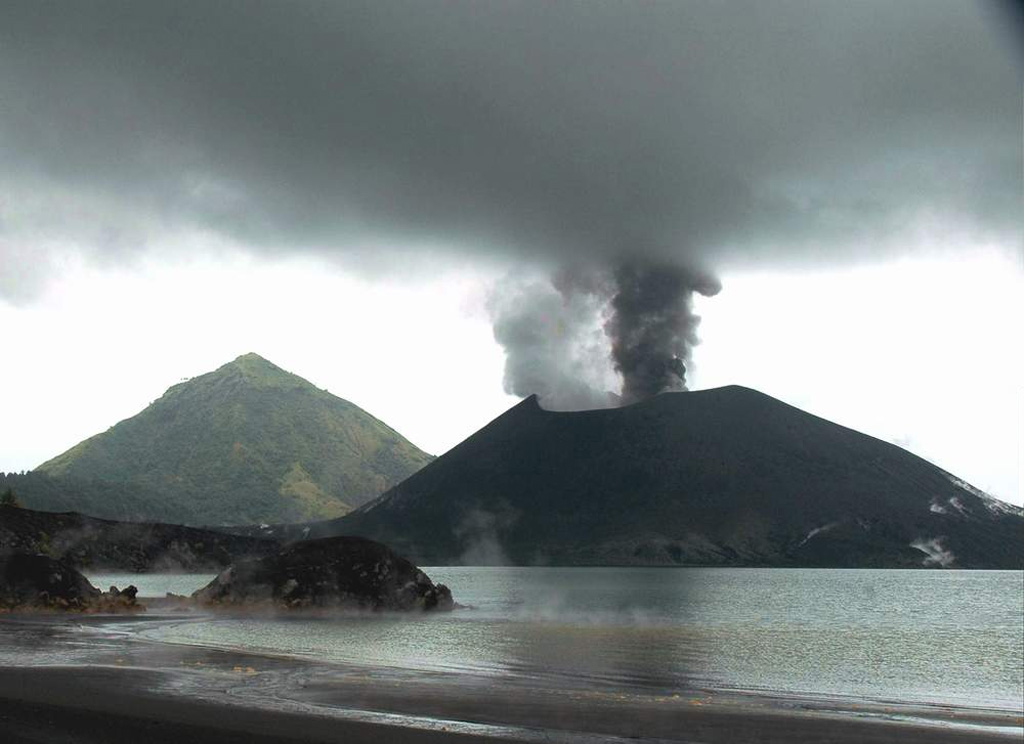 Tavurvur cone at Rabaul is seen in eruption in this 25 May 2005 view looking from the NW across Matupit Harbor. Two plumes, one white and the other dark gray, are originating from separate vents. Intermittent small-to-moderate explosive eruptions took place throughout much of the year. The conical peak in the background is Turanguna. Photo by Roy Price, 2005 (University of South Florida).