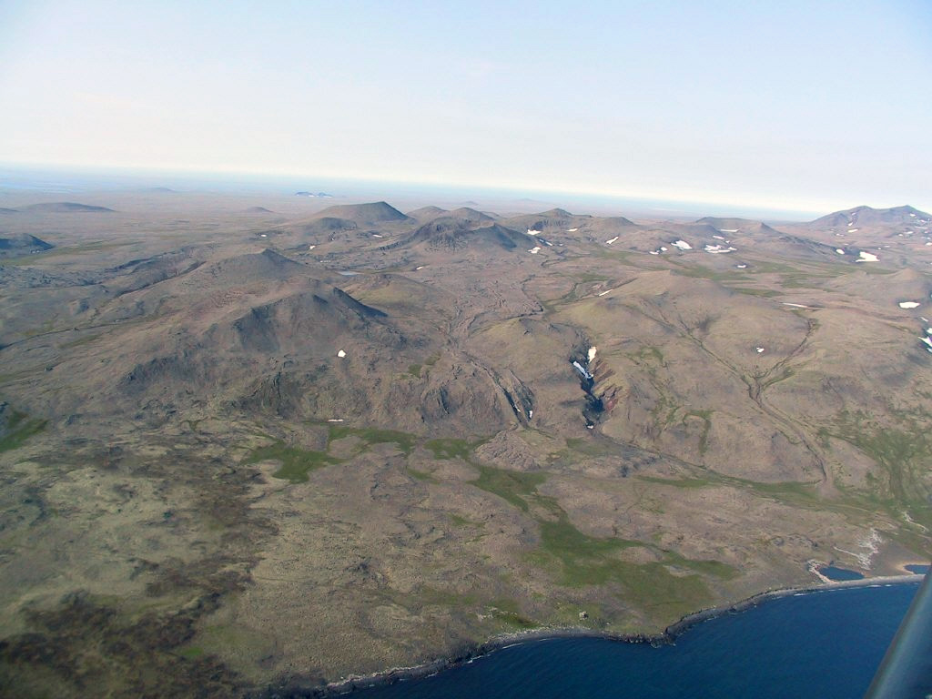 Pyroclastic cones dot the surface of the Kookooligit Mountains in north-central St. Lawrence Island in the Bering Sea.  Kookooligit is a 30 x 40 km wide, 673-m-high shield volcano of Pleistocene-to-Holocene age overlain by more than 100 small cinder cones, most of which are aligned E-W along the crest of the elongated shield volcano.  The cones were the source of dominantly alkali basaltic and basanitic lavas flows.       Photo by Bob Webster.