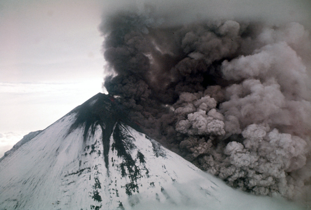 An ash plume rises above the surface of a pyroclastic flow descending the flanks of Pavlof on the Alaska Peninsula in 1975. Incandescent lava can be seen on the upper cone. Intermittent phreatomagmatic to magmatic eruptions began 13 September 1975 and continued until at least March 1977. Possible lava flows or lahars were reported in October 1975 and December 1976. Photo by U.S. Geological Survey, 1975.