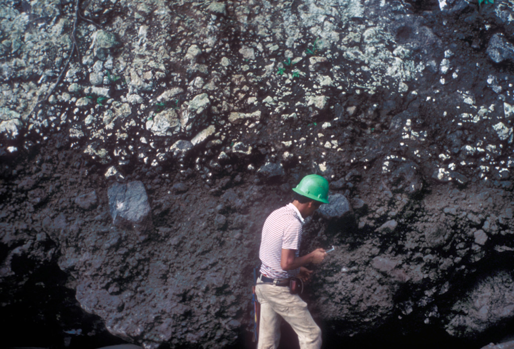 Geologist Eric Fernandez examines an outcrop of pyroclastic rocks along the banks of the Río Genio, on the northern side of Cocos Island.  Pyroclastic rocks were erupted either immediately prior to or contemporaneously with trachytic rocks forming a lava dome.  Pyroclastic rocks are thickest on the northern side of the island, which may represent the topographic high of the old seamount. Photo by Pat Castillo, 1984 (Scripps Institution of Oceanography, University of California San Diego).