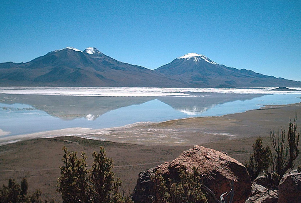 Arintica (left) and Puquintica volcanoes are reflected in the Salar de Surire.  Volcán Arintica is the central and most prominent cone of a large volcanic complex that rises north of the Salar de Surire.  The volcanoes are extensively dissected, but the latest activity at 5597-m-high Arintica produced a possible postglacial lava flow from a relatively well-preserved summit crater that descended the SE flank, but the age of the volcano is not known precisely.  Cerro Puquintica (Poquentica) is considerably older than Arintica and rises to 5760 m.   Photo by Eduardo Bascuñán, 2005.