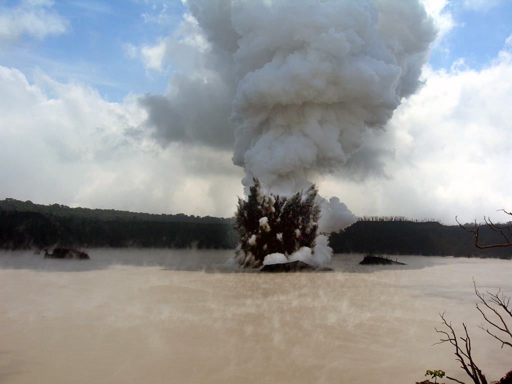 An explosive eruption from Lake Voui at Ambae on 4 December 2005 seen looking approximately E from the crater rim. A dark cock’s-tail plume and a lighter gas-and-ash plume can be seen rising above the vent within the late. Three small islands that formed prior to this eruption can also be distinguished. Photo by Philipson Bani, 2005 (Institut Recherche Développement, IRD).
