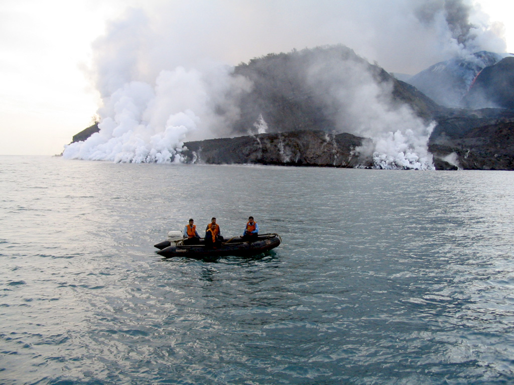 A lava flow enters the sea along the W coast of Barren Island on 21 July 2005. The flow entered the sea at two points following the routes of the previous 1991 and 1994-95 lava flows. A plume from the summit crater of the central scoria cone is visible to the upper right, along with an active lava channel descending the flanks. Photo courtesy of Indian Coast Guard, 2005.