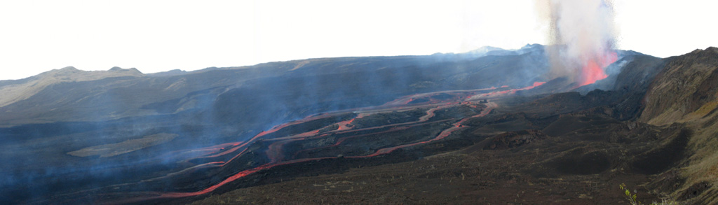 This composite view looks west from the NE rim of Sierra Negra's caldera (right) on October 23, 2005.  The caldera floor is to the left.  Four active vents are superimposed in this photo, aligned along the E-W fracture that lies at the base of the inner caldera wall.  Numerous lava flows descended southwards to the left where they joined to form one single flow of a'a lava ~ 1 km wide and 7 km long that had already reached the southern inner wall of the caldera on the 23rd. Photo by Minard Hall, 2005 (Escuela Politecnica Nacional, Quito).