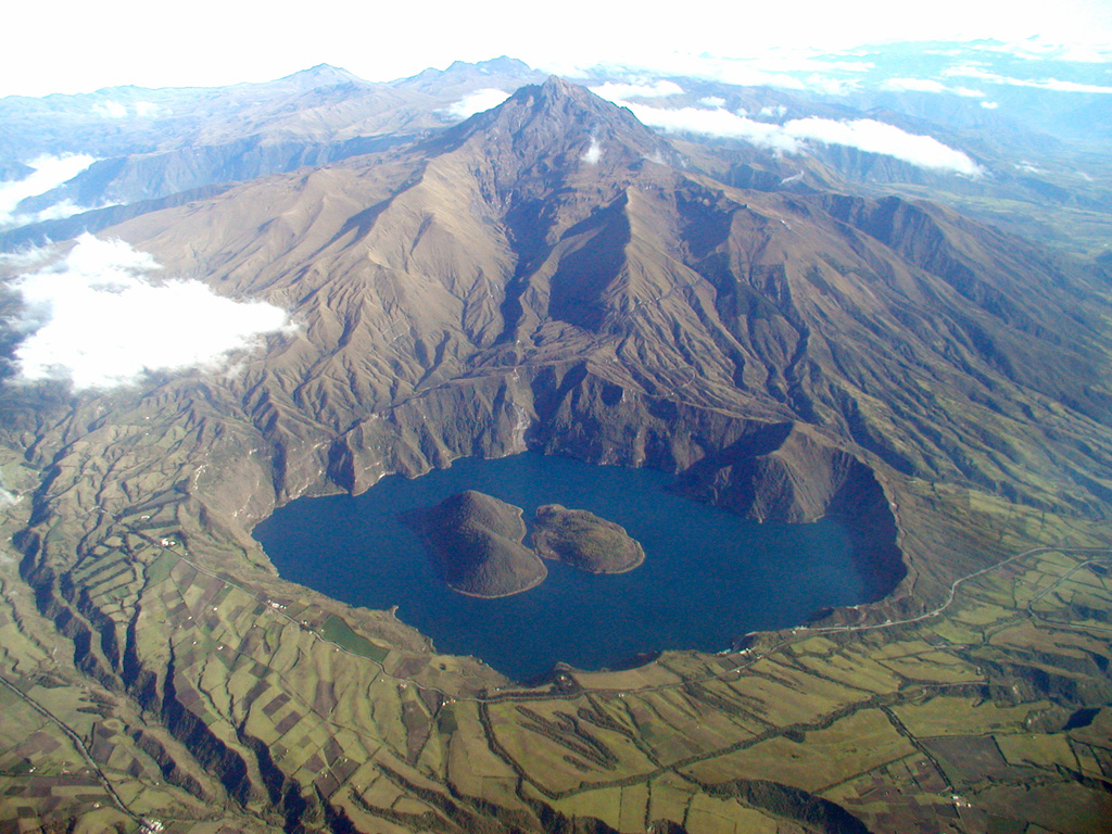 The scenic lake-filled Cuicocha caldera is located at the southern foot of the sharp-peaked Pleistocene Cotacachi stratovolcano (top center) about 100 km north of Quito.  Farmer's fields encroach on the rim of the 3-km-wide caldera, which was created during a major explosive eruption about 3100 years ago.  Dacitic lava domes form two forested islands in the caldera lake.  Pyroclastic-flow deposits from the caldera-forming eruptions cover wide areas in now populated areas below the low-rimmed caldera.      Photo by Patricio Ramon, 2003 (Instituto Geofisca, Escuela Politecnica Nacional).
