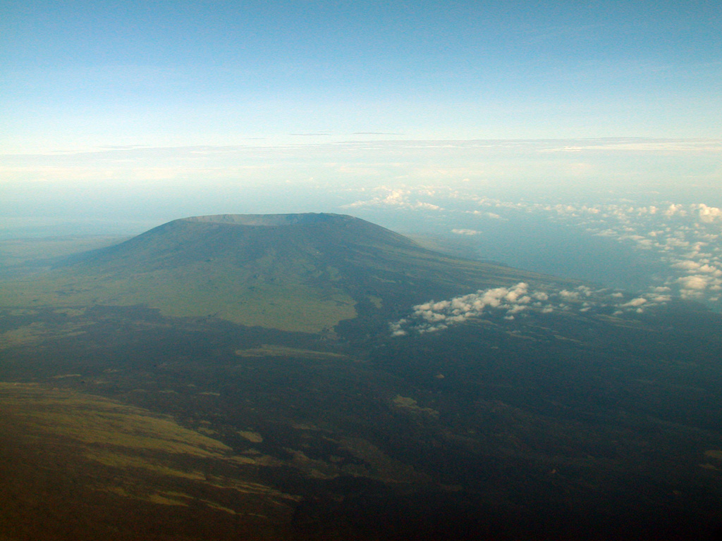 The caldera of Cerro Azul volcano is seen from the east, with the slopes of Sierra Negra volcano in the foreground.  The steep-walled 4 x 5 km nested summit caldera complex is 650 m deep.  Dark-colored, fresh-looking lava flows erupted from NE flank vents can be seen at the right, and a SE flank fissure erupted in 1998, producing a lava flow that reached to within 2 km of the coast.  Photo by Patricio Ramon, 2003 (Instituto Geofisca, Escuela Politecnica Nacional).