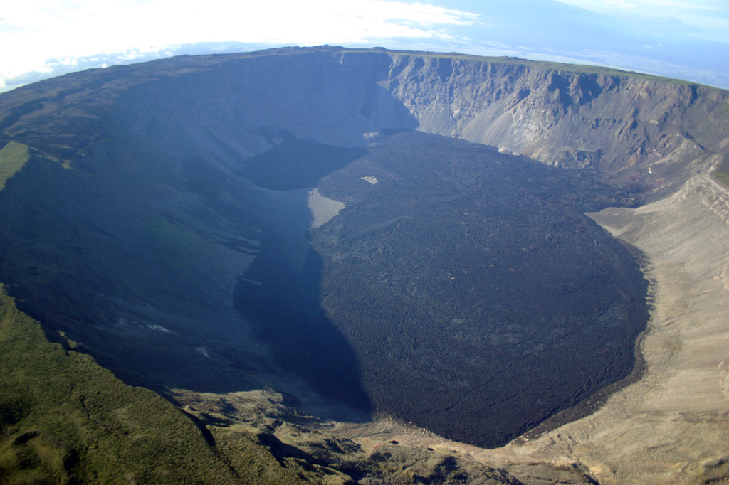An aerial view from the north looks across the 6 x 7 km wide summit caldera of Volcán Wolf.  Fresh-looking, dark-colored lava flows, erupted from fissures on the eastern and western caldera walls, cover much of the caldera floor.  At 1710 m, Wolf is the highest of the Isabella Island shield volcanoes. Photo by Patricio Ramon, 2005 (Instituto Geofisca, Escuela Politecnica Nacional).