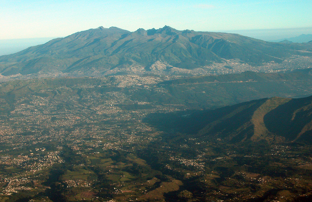 An aerial view from the east shows the Pichincha volcanic complex, one of Ecuador's most active volcanoes, rising immediately above the capital city of Quito.  Guagua Pichincha (left) and the sharp-topped Pleistocene Rucu Pichincha stratovolcano (right) form a broad volcanic massif overlooking Ecuador's largest city.  The largest historical eruption from Guagua Pichincha took place in 1660 CE, when ash fell over a 1000 km radius, accumulating to 30 cm depth in Quito.   Photo by Patricio Ramon, 2004 (Instituto Geofisca, Escuela Politecnica Nacional).