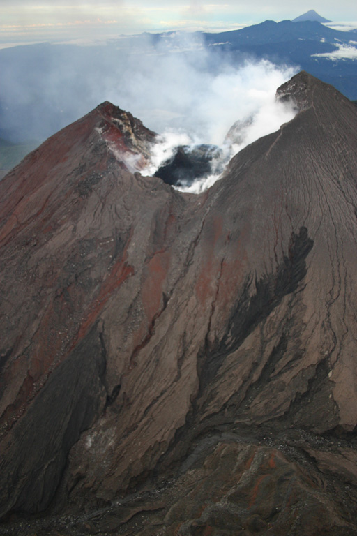 The steaming summit crater of Reventador volcano in northern Ecuador is seen in this aerial view from the north on April 21, 2005.  The black area in the center of the crater is a new lava dome that began growing inside the crater during an eruption that had begun in November 2004.  Lava flows from the crater periodically descended a notch in the far crater wall and flowed down the southern flank of the cone.  Conical Sumaco volcano is seen in the background. Photo by Patricio Ramon, 2005 (Instituto Geofisca, Escuela Politecnica Nacional).