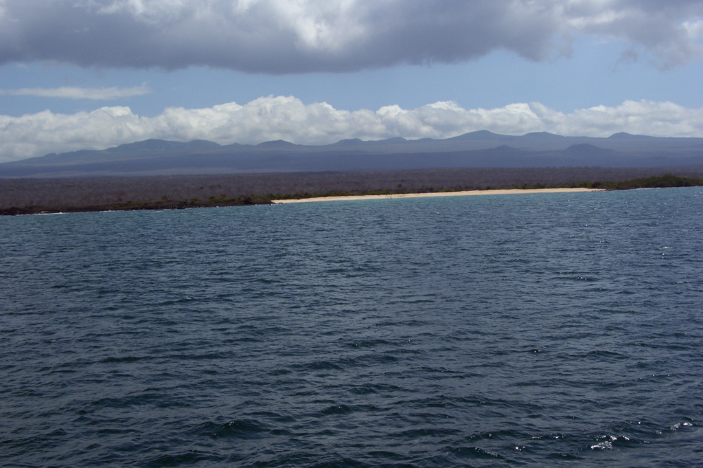 The broad shield volcano forming Santa Cruz Island is seen from its northern coast.  The oval-shaped, 32 x 40 km wide island is capped by cinder cones with well-preserved craters that largely bury a shallow summit caldera.  The highland scoria cones are grouped along an E-W belt parallel to recent fault scarps that border Academy Bay, location of the Charles Darwin Research Station.   Photo by Lee Siebert, 2006 (Smithsonian Institution).