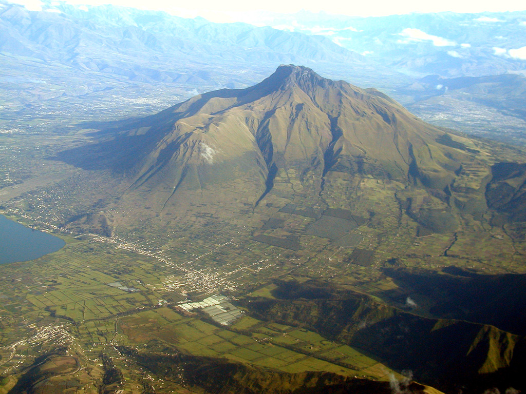 Imbabura volcano rises above the town of San Pablo del Lago in this aerial view from the south.  The tip of Laguna de San Pablo is visible at the left.  The main edifice, Taita Imbabura ("Father Imbabura"), forms the summit.  Huarmi Imbabura ("Imbabura's Son") is a lateral lava-dome complex forming the grassy shoulder on the SW flank directly above the town of San Pablo del Lago in this view.   Activity at the dominantly Pleistocene Imbabura volcano continued into at least the early Holocene. Photo by Patricio Ramon (Instituto Geofisca, Escuela Politecnica Nacional).