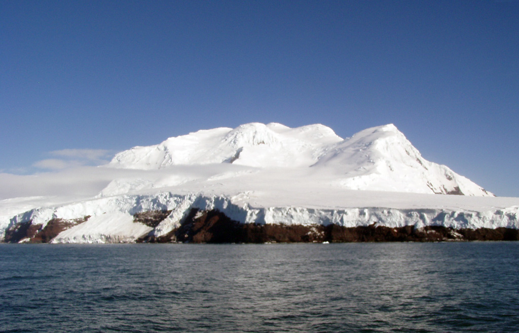 Peter I Island, located in the Bellingshausen Sea opposite Ellsworth Land, is seen here from the north showing the Lars Christiansen Peak. This volcanic island has a steep coastline and is more dissected on the northern side, with a broader more gentle slope to the south. The most recent dated activity occurred about 100,000 years ago. Photo by Melvin Vye, 2006.