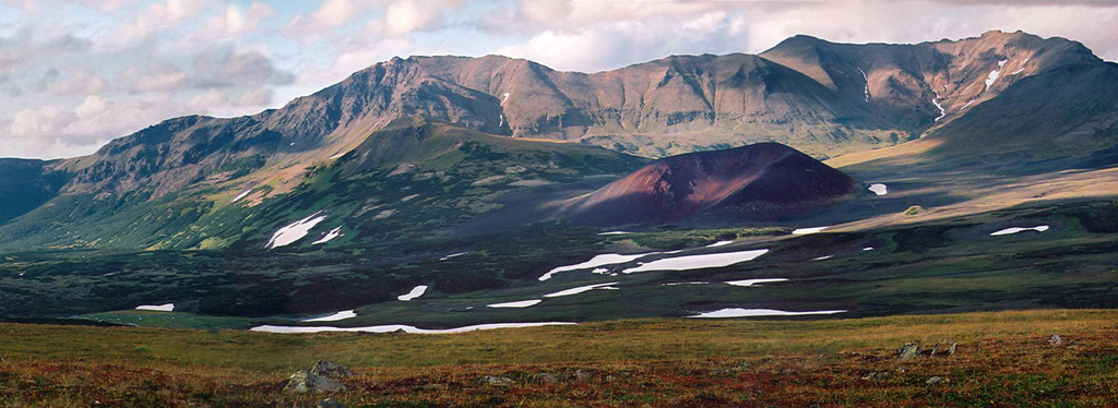 The red Tobeltsen scoria cone, seen from the SE, lies on the lower WSW flank of Severny erupted about 3,500 years ago and was the source of lava flows that descend diagonally to the lower left. Severny is a late-Quaternary volcano located at the NW end of a major NE-trending graben along the crest of the northern Sredinny Range. Copyrighted photo by Maria Pevzner, 2005 (Russian Academy of Sciences, Moscow).