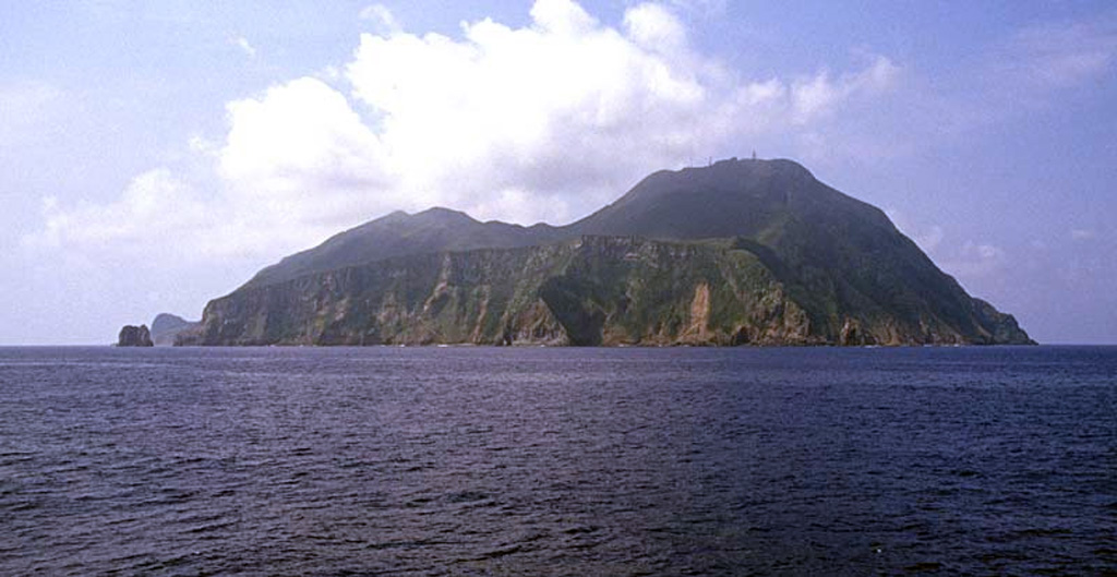 Akusekijima is seen from the N with the Omune lava flow forming a plateau in the foreground. The dacitic lava flow, the youngest featute, has experienced little erosion and lacks overlying tephra layers, suggesting a young age. Akusekijima is located in the southern Ryukyu Islands, and consists of the two older Biroyama and Nakadake edifices. The Mitake lava dome (right) forms the high point of the small 2.5 x 3.2 km island. Copyrighted photo by Shun Nakano, 2004 (Japanese Quaternary Volcanoes database, RIODB, http://riodb02.ibase.aist.go.jp/strata/VOL_JP/EN/index.htm and Geol Surv Japan, AIST, http://www.gsj.jp/).