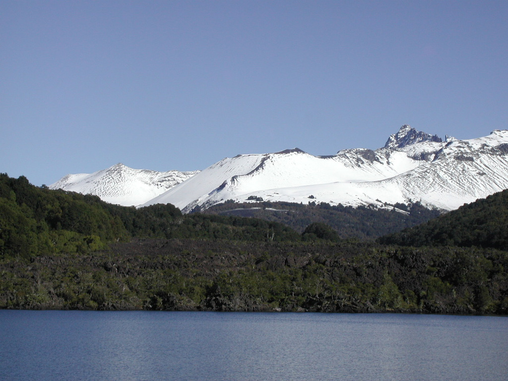 The blocky, partially forested Escorial lava flow in the foreground is seen from the north on a boat on Lago Epulafguen.  The flow originated from the Achín-Niellu pyroclastic cone (center), which is part of the Huanquihué group of young basaltic volcanoes in Argentina near the Chilean border south of Lanín volcano.  The Escorial lava flow was erupted about 200 years ago, and local residents recount oral histories of the eruption, which was observed by their grandparents.   Photo by Héctor Osvaldo González, 2007.