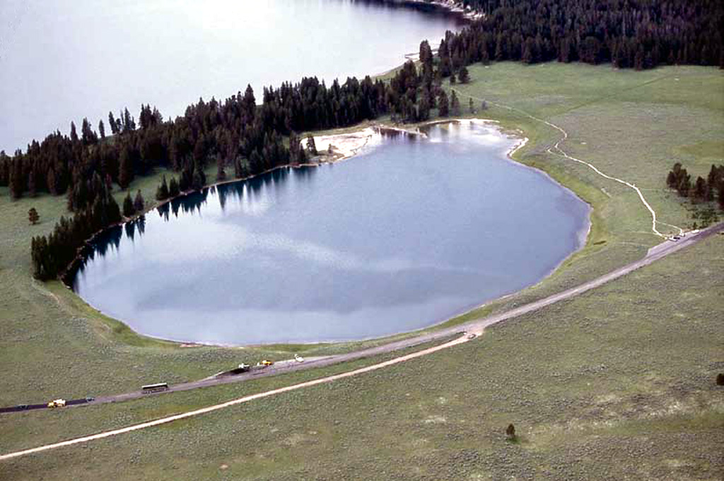 The 500-m-wide Indian Pond hydrothermal explosion crater immediately north of the NE shore of Yellowstone Lake formed about 3350 years ago.  Deposits from this eruption extend 3 km from the crater and are up to 3-4 m thick.  Yellowstone Lake is seen at the top, with the highway leading to Cody at the bottom in this aerial view from the NE. Photo by Jim Peaco, 2001 (National Park Service).