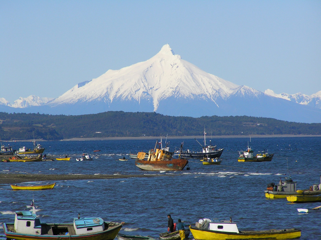 The dramatic summit spire of Corcovado volcano is seen in this telephoto view from the west from the town of Quellon on the island of Chiloe.  The volcano rises across the Gulf of Corcovado, which lies beyond the ridge in the middle distance.  The main edifice at Corcovado is likely Pleistocene in age, but historical eruptions have been reported, probably from Holocene cinder cones surrounding the volcano. Photo by Bryan Freeman, 2005.
