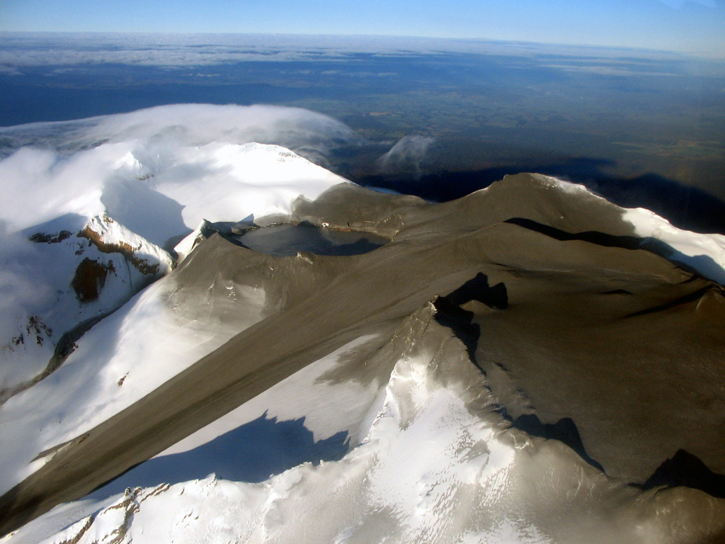 An aerial view of the summit of Ruapehu from the NE on 26 September 2007 show the effect of a brief eruption the previous day. The eruption originated from Crater Lake (left-center), and ejected ash and mud that covered much of the summit area. A large lahar swept down the Whangaehu glacier to the left and a smaller lahar exited the low point on the rim of Crater Lake and descended the narrow gully above the larger lahar. Photo courtesy of GeoNet, 2007 (Global Volcanism Network Bulletin).