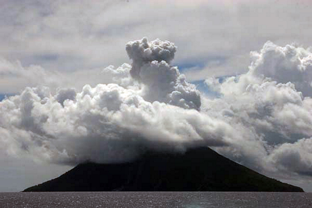 A plume rises above meteorological clouds over Tinakula volcano on 21 February 2006. Tinakula had resumed eruptive activity earlier that month. Photo by Bill Yeaton, 2006.