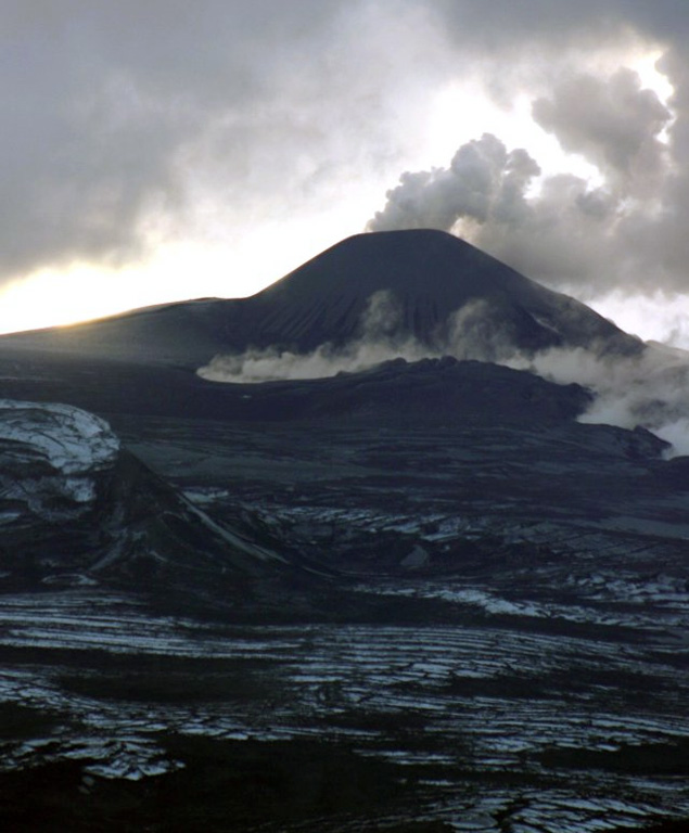 This 13 January 2006 view of the north side of Montagu Island shows the lava field formed by a recent eruption. A plume rising above Mount Belinda appears to be dominantly composed of steam. The snaking plume of steam in front of the cone likely indicates the location of hot lava flow. There was no record of Holocene activity at Montagu until satellite data, beginning in late 2001, revealed thermal anomalies consistent with lava lake activity. Photo courtesy of Dave Hall, Frikkie Viljoen and Ian Hunter, 2006 (SA Argulhas and South African Weather Service).