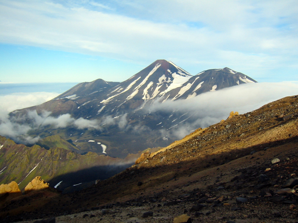 The three E-W-trending summit cones of the Tanaga volcanic complex, Sajaka, Tanaga, and East Tanaga (from left to right) are seen from the summit of Takawangha volcano. Tanaga is the central and highest of three at the NW tip of Tanaga Island. The ridge to the lower left is part of a caldera rim that formed by the collapse of an ancestral Tanaga edifice during the Pleistocene. Photo by Michelle Coombs, 2003 (Alaska Volcano Observatory, U.S. Geological Survey).