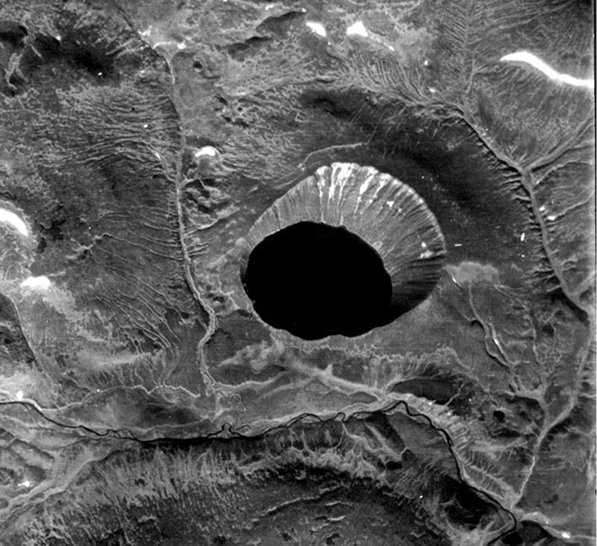 Kinenin maar is seen in this near-vertical aerial photo, with the lake reaching 1 km in diameter. The maar was named after the Kinenin River seen to the south, and was formed during an explosive eruption about 1,100 years ago. The NE crater wall is significantly higher and coincides with the dominant direction of the tephra dispersal.  Photo from Holocene Kamchataka volcanoes (http://www.kscnet.ru/ivs/volcanoes/holocene/main/main.htm).