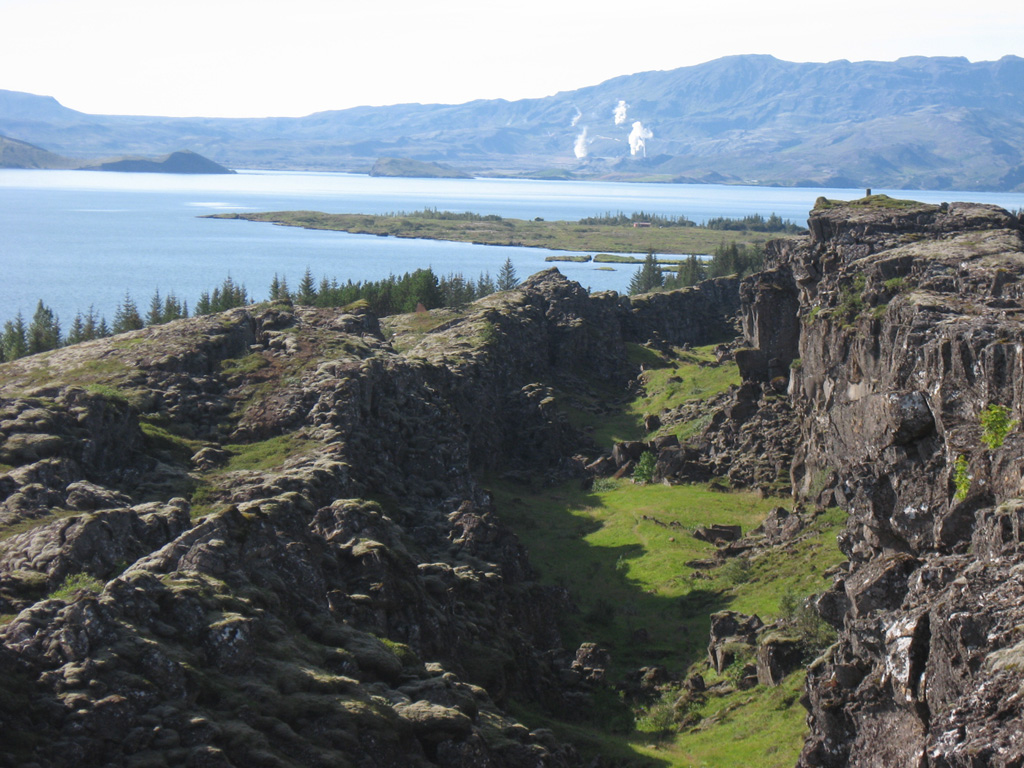 The Hengill central volcano in the right background rises above Thingvallavatn lake as seen from Thingvellir, the historical site of the Icelandic parliament. Steam clouds rise from the Nesjavellir geothermal area in this view from the northeast. Graben structures in the foreground cut the Thingvallahraun lava flow in the foreground, which was erupted about 10,000 years ago. The cone in the lake on the left is Sandey, a tuff ring formed in a phreatomagmatic eruption about 1,900 years ago. Photo by Lee Siebert, 2008 (Smithsonian Institution).