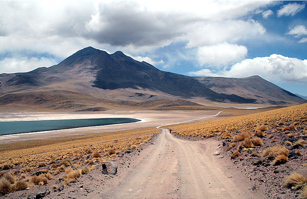 The broad Volcán Miñiques massif rises to the SE above Laguna Miñiques.  The 5910-m-high summit of the volcano is cut by three overlapping, E-W-trending craters.  Larger craters, partially filled by lava domes and flows, are located west and NE of the summit of the volcano, which is of late Pleistocene or Holocene age.  A prominent lava flow, not visible in this image, extends NW-ward from the summit to the lower flanks, separating Laguna Miñiques from Laguna Miscanti to the north.   Photo by Jos Offermans, 2008.