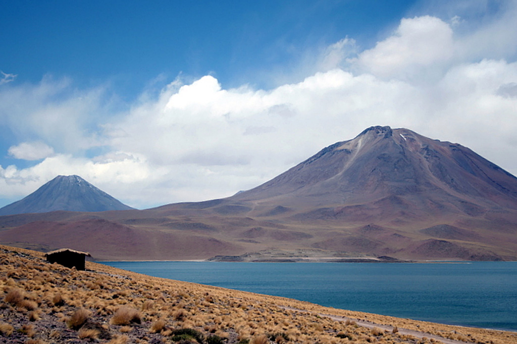 Conical Volcán Chiliques (left) and Volcan Miscanti (right) rise to the NE above Laguna Miscanti.  The 5778-m-high summit of Chiliques contains a 500-m-wide crater, and some youthful lava flows may be of Holocene age. This volcano had previously been considered to be dormant; however, in 2002 a NASA nighttime thermal infrared ASTER satellite image showed low-level hot spots in the summit crater and upper flanks.  Miscanti volcano is of probable late-Pleistocene age.  Photo by Jos Offermans, 2008.