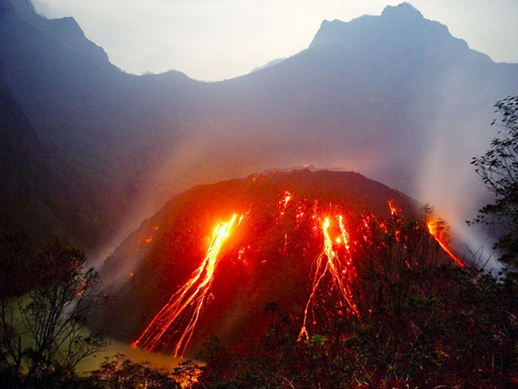 Incandescent blocks from the growing lava dome at Kelud volcano in November 2007 form traces extending into the crater lake (lower left) in this view from the west. Increases in water temperature and color were noted beginning on 11 September 2007. On 4 November a lava dome was seen rising above the lake surface and reached a visible radius of 250 m and a height of 120 m by 8 November. Dome growth had apparently ceased by April 2008, by which time it had filled much of the crater lake. Copyrighted photo by Tom Pfeiffer, 2007.