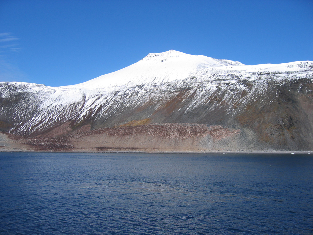 Paulet Island, seen here from the northwest, is a 1.8 x 2.2 km island located east of the tip of Graham Land Peninsula. A basal sequence of horizontal lava flows exposed in steep cliffs is capped by a well-preserved cinder cone complex (top center) with a small distinct summit crater. The darker brownish areas near and above the shoreline at the center of the photo are Adelie penguin colonies. Photo by Jeff Post, 2007 (Smithsonian Institution).