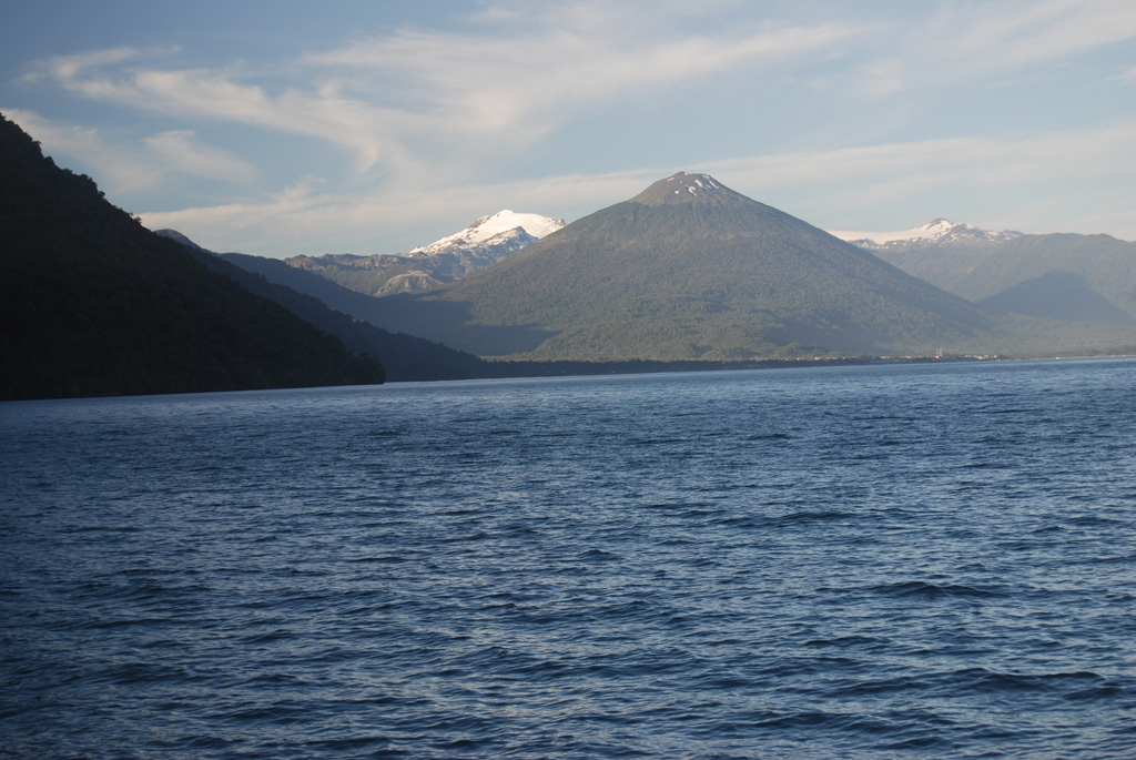 Symmetrical forested Volcán Hornopirén is seen from the SW from a ferry approaching the town of the same name at the head of a fjord at the NE end of the Gulf of Ancud.  The 1572-m-high volcano, whose name means "snow oven," lies along a graben defined by the major regional Liquiñe-Ofqui fault zone.  The volcano was said to be in eruption in 1835, although no details are known.  Glacier-capped Yate volcano appears in the background to the left of Hornopirén.      Photo by Jon Major, 2011 (USGS, Cascades Volcano Observatory).