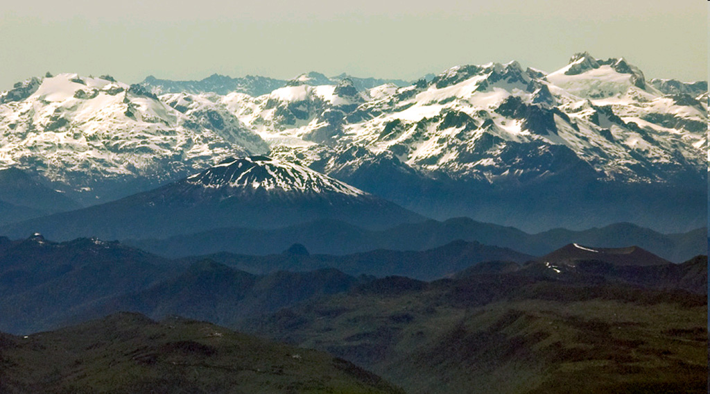 The sparsely vegetated pyroclastic cone at the lower right with a strip of snow on its crater rim is Volcán Apagado, also known as Hualiaque.  Seen in an aerial view from the NW with the rugged snow-capped Chilean Andes in the background, it lies in the center of the peninsula between the Gulf of Ancud and the Reloncaví estuary. The pyroclastic cone lies within a 6-km-wide depression breached to the SW.  The broad symmetrical Hornopirén volcano, capped by snow fields, lies to the east of Apagado at the left center.    Photo by Gerald Prins, 2008 (Wikimedia Commons).