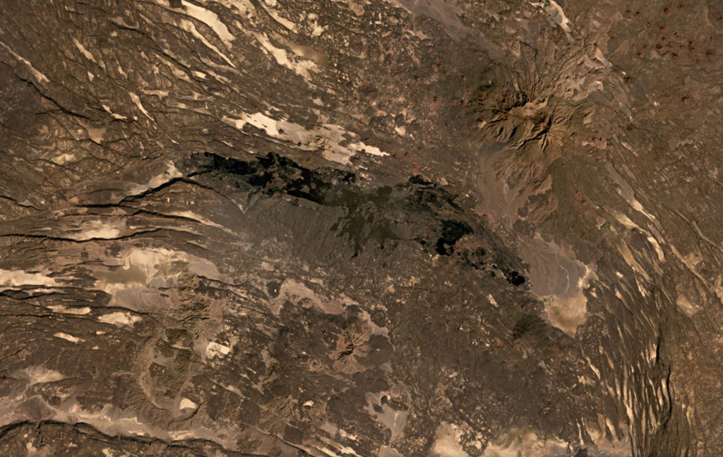 The roughly 40-km-long darker lava flows extending across the center of this December 2020 Planet Labs satellite image monthly mosaic (with N at the top) were produced by the western Manda portion of the Manda-Inakir complex and fill a graben formed through faulting. This complex represents a failed rift segment along the Ethiopia-Djibouti border. Mousa Alli is the edifice to the NE; this image is approximately 80 km across. Satellite image courtesy of Planet Labs Inc., 2020 (https://www.planet.com/).