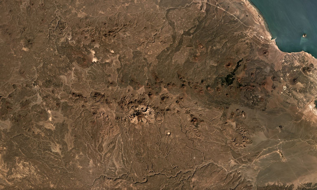 The chain of scoria cones and lava flows extending along an E-W trend in this December 2019 Planet Labs satellite image mosaic is the Assab volcanic field near the Red Sea coast in southern Eritrea (N is at the top; this image is approximately 58 km across). This field covers an area roughly 55 x 90 km, with lava flows reaching the Red Sea to the E, including to the coastal city of Assab. Satellite image courtesy of Planet Labs Inc., 2019 (https://www.planet.com/).