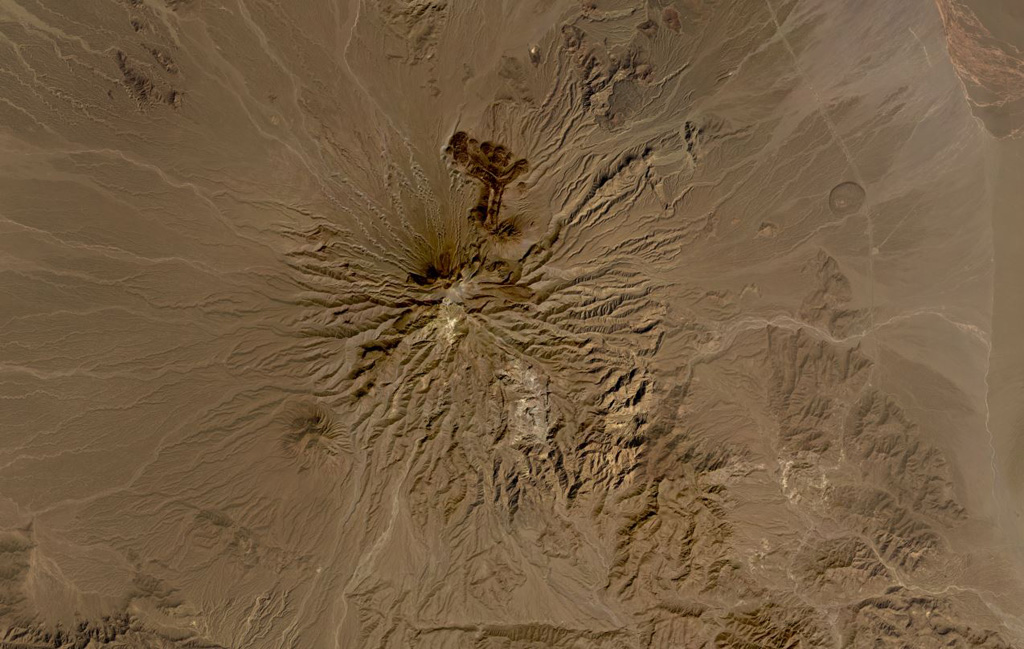 Bazman volcano is part of the Makran arc in SE Iran, shown here in this October 2019 Planet Labs satellite image monthly mosaic (N is at the top; this image is approximately 44 km across). Scoria cones and lava flows have formed across the eroded flanks, with several darker lava flows containing levees and lobate flow fronts visible on the northern flank. The Bazman granitoid complex forms part of the southern flank and formed between 83 and 72 million years ago. Satellite image courtesy of Planet Labs Inc., 2019 (https://www.planet.com/).