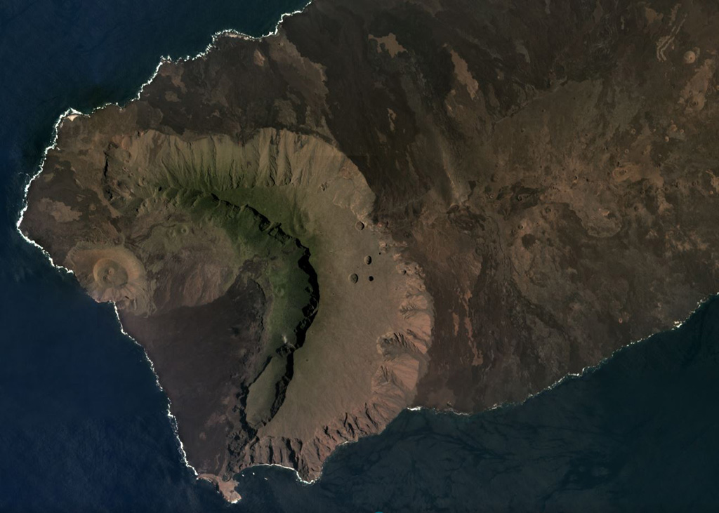 The western side of Volcán Ecuador has formed through caldera collapse and subsequent flank collapse, producing the caldera that opens towards the ocean in this March 2019 Planet Labs satellite image monthly mosaic (N is at the top; this image is approximately 13 km across). Within the caldera is the Cerro Grande tuff cone along the coast, a slump block along the SE caldera wall, and lava flows, as well as smaller vents. The East Rift is to the right in this image, towards Volcán Wolf out of view. Satellite image courtesy of Planet Labs Inc., 2019 (https://www.planet.com/).
