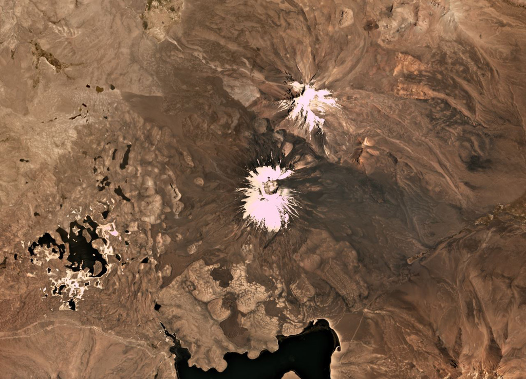 Parinacota is the larger of the two main edifices in this November 2019 Planet Labs satellite image monthly mosaic (N is at the top; this image is approximately 23 km across). With Pomerape to the NE, together they form the Nevados de Payachata group along the Chile-Bolivia border. The group of lakes to the SW formed within a debris avalanche deposit about 8,000 years ago that is more than 22 km long with a volume of 6 km3. The current cone formed over the resulting scarp and older edifice, and has a summit crater around 650 m wide. Lava flows are visible on all flanks, with some flows emplaced around the debris avalanche deposit hummocks. Satellite image courtesy of Planet Labs Inc., 2019 (https://www.planet.com/).