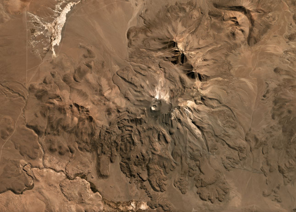 The flanks of Isluga volcano in Chile are formed by numerous lobate lava flows visible in this June 2019 Planet Labs satellite image monthly mosaic (N is at the top; this image is approximately 23 km across). The lavas have lateral levees and pressure ridges especially visible on the southern flanks. The most recent 400-m-diameter summit crater is visible at the western side of the summit area. Satellite image courtesy of Planet Labs Inc., 2019 (https://www.planet.com/).