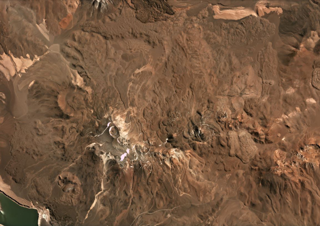 The Falso Azufre volcanic complex, covering 387 km2 at the Chile-Argentina border, was constructed largely by lava flows up to 7 km long and 4 km wide, shown in this April 2019 Planet Labs satellite image monthly mosaic (N is at the top; this image is approximately 22 km across). The crater of the Kunstmann edifice is in the upper left corner, and the eastern domes, coulees, and lava flows are to the far right. The summit region craters are aligned along a NW-SE trend to the W (the Falso Azufre edifice), and along a ENE-WSW trend on the eastern side (the Dos Conos edifice). Satellite image courtesy of Planet Labs Inc., 2019 (https://www.planet.com/).
