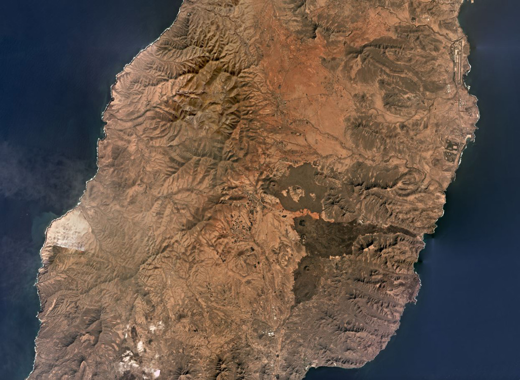 Fuerteventura island comprises the Northern, Central, and Southern Volcanic Complexes, with the Central complex shown in this November 2019 Planet Labs satellite image monthly mosaic (N is at the top; this image is approximately 42 km across). There was a period of significant erosion and quiescence before scoria cones and smaller lava flows were produced during the Quaternary through to recent times, including the darker lava flows and cones near the center of this image. Satellite image courtesy of Planet Labs Inc., 2019 (https://www.planet.com/).