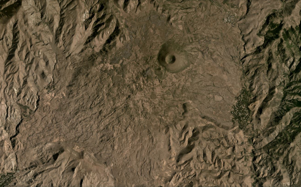 The Vaiyots-Sar scoria cone has a roughly 500-m-wide summit crater, seen in this August 2020 Planet Labs satellite image monthly mosaic (N is at the top; this image is approximately 15 km across). Lavas with visible flow boundaries and levees are to the NW and S to SW of the cone, with some long, linear flows and some much broader flow fronts with pressure ridges. Satellite image courtesy of Planet Labs Inc., 2020 (https://www.planet.com/).