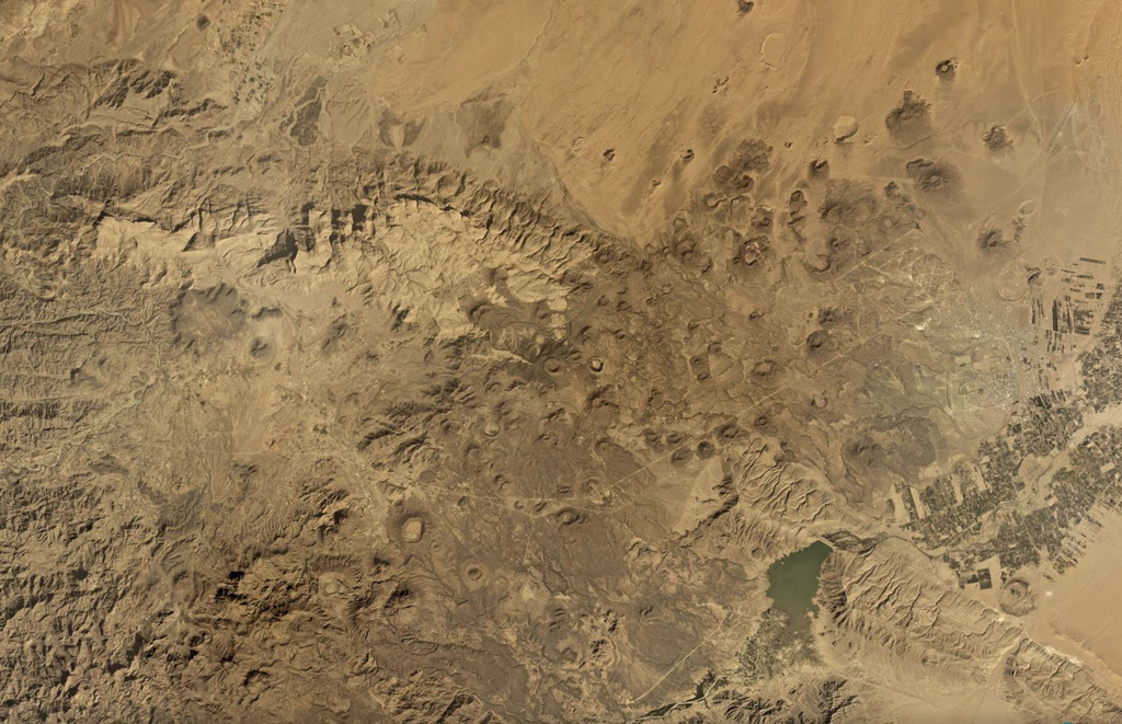 The Jabal Haylan volcanic field comprises scoria cones and tuff rings and associated lava flows across a 75-km-long area, with a portion of the field shown in this Planet Labs satellite image monthly mosaic (N is at the top; this image is approximately 52 km across). The chain crosses a NW-SE-trending fault that with visible offset in this image. Many of the cones and rings have experienced flank collapse, rafting, or erosion, leaving amphitheater-shaped craters. Some tuff rings appear to have lava domes that have formed within the crater. Satellite image courtesy of Planet Labs Inc., 2019 (https://www.planet.com/).