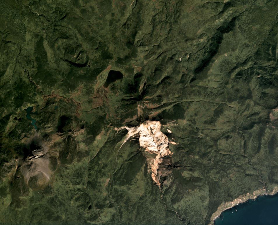 The vegetated summit of Odamoisan (also called Tebenkov) is in the center of this September 2019 Planet Labs satellite image monthly mosaic (N is at the top; this image is approximately 9 km across). South of the summit is the unvegetated Machekh crater with continuing geothermal activity. The unvegetated cone to the SW is Etorofu-Yakeyama, or the Grozny Group. Satellite image courtesy of Planet Labs Inc., 2019 (https://www.planet.com/).