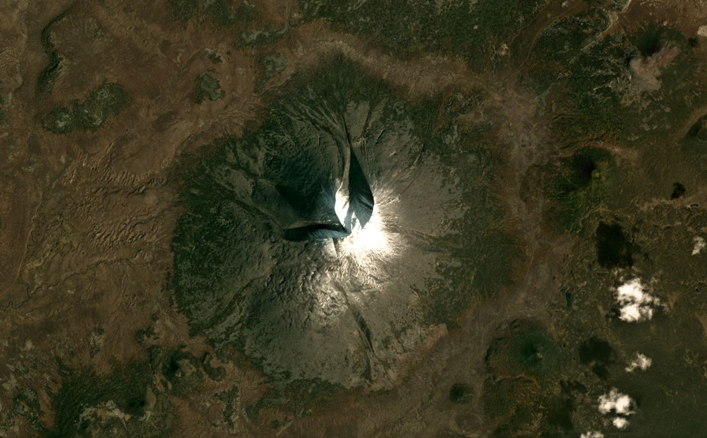 The Anaun edifice has several erosional ravines on the northern and western flanks that extend from the summit, seen in this September 2019 Planet Labs satellite image monthly mosaic (N is at the top; this image is approximately 15 km across). Smaller scoria cones have formed around the cone, like the one to the E with a summit crater. Satellite image courtesy of Planet Labs Inc., 2019 (https://www.planet.com/).