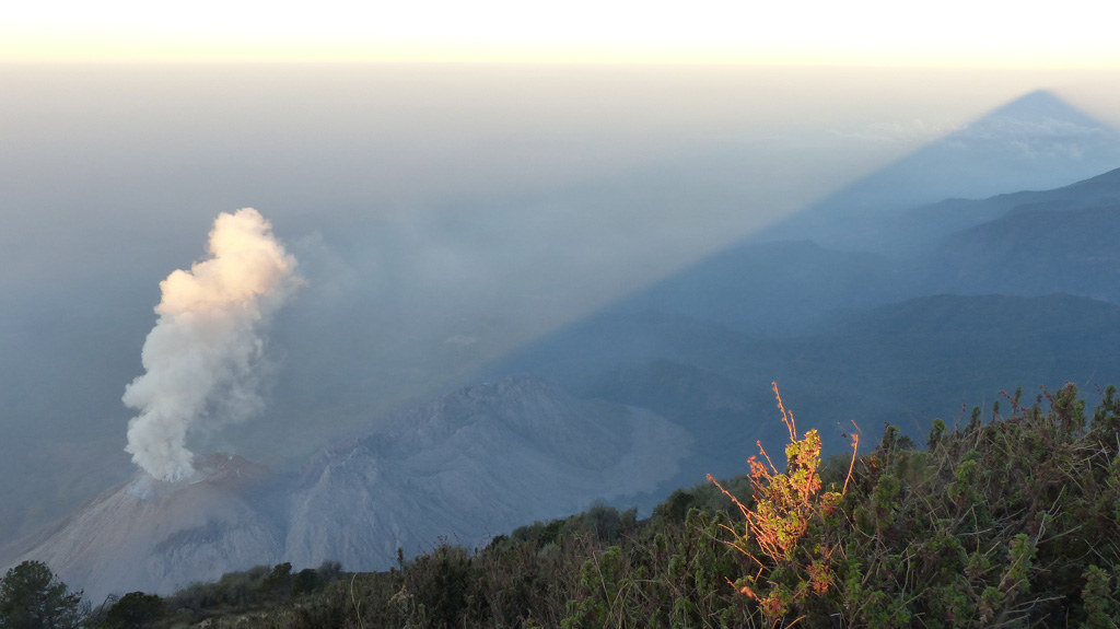 This February 2017 view of El Caliente of the Santiaguito lava dome complex is from the Santa Maria summit (producing the shadow to the right). The other Santiaguito domes visible from left to right (approximately NE-SW) are El Caliente, La Mitad, El Monje, and El Brujo. El Caliente is degassing through its characteristic ring-shaped fracture network. Photo by Ailsa Naismith, 2017.