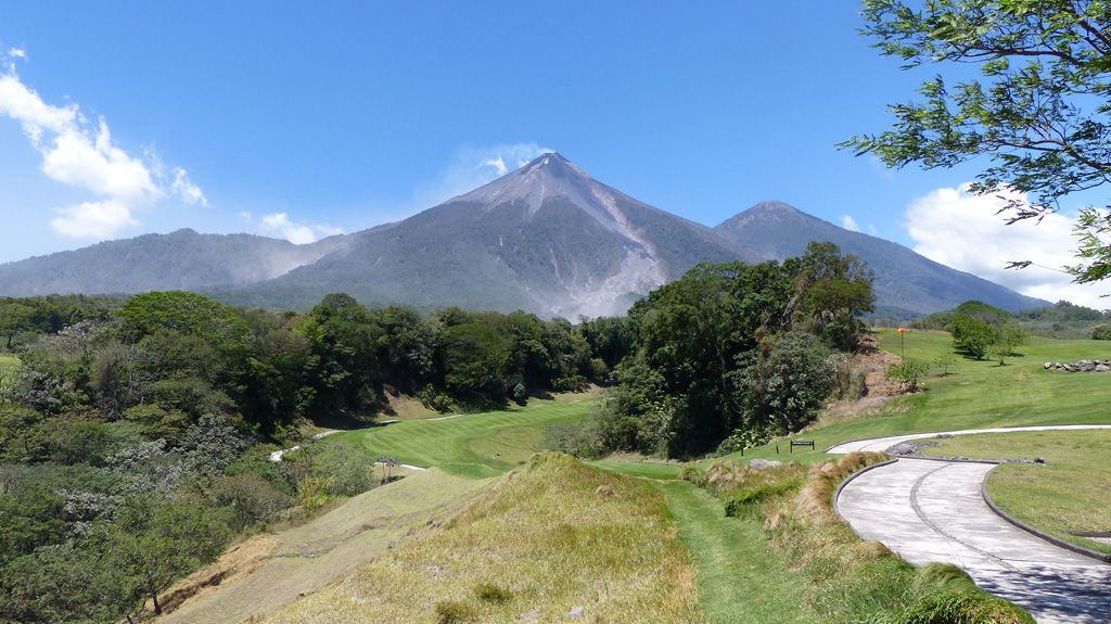 Fuego (left) and Acatenango (right, behind) are seen here from La Reunion Golf Resort and Residences below the SE flank in March 2017. Barranca Las Lajas is the ravine from the summit down the flank, containing eruption deposits from the frequent activity. Weak degassing from the summit is producing a faint plume dispersing towards the SW. Photo by Ailsa Naismith, 2017.