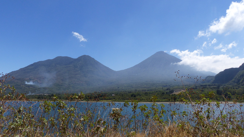 This 2018 view of Volcán Tolimán (left) and Volcán Atitlán (right) is from the shores of Lake Atitlan opposite the town of Santiago Atitlan (just out of view to the left). The cones formed along the southern rim of the Atitlán III caldera with the lake in the foreground filling the northern area. Photo by Ailsa Naismith, 2018.